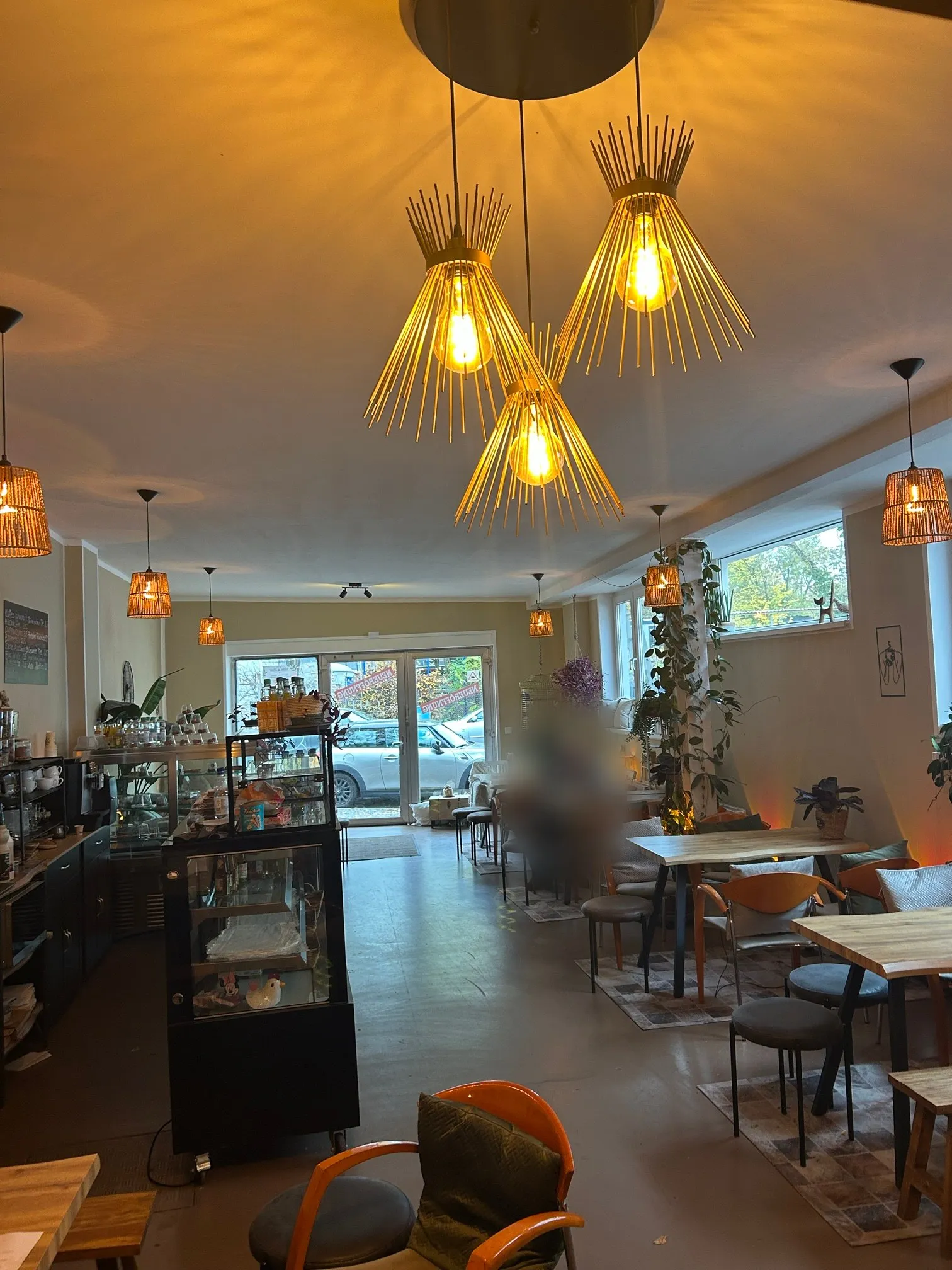 Der Café-Raum mit Holztischen, Pflanzen und goldenen Lampen