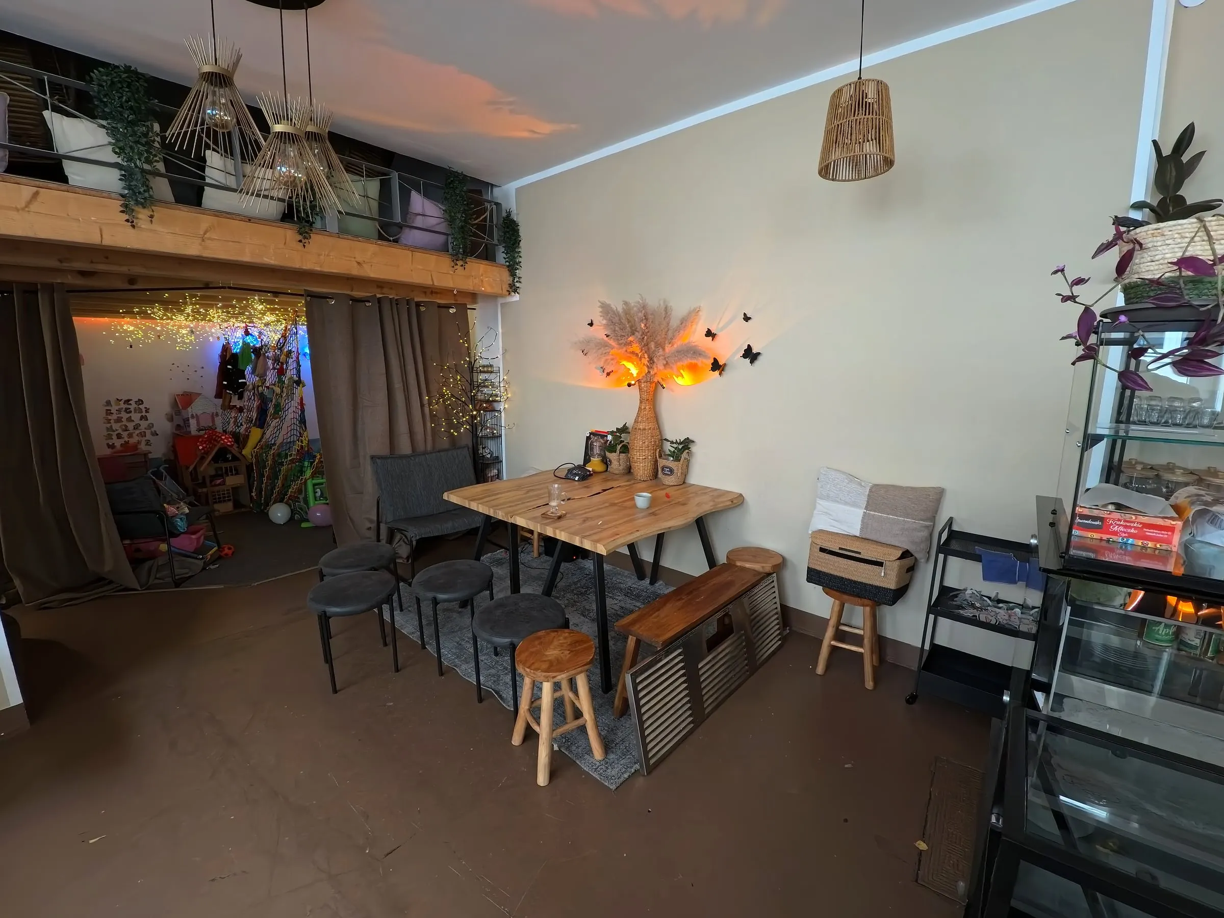 Der hintere Teil des Cafés mit Holztisch, Hockern und dem Eingang zur Spielecke unter der Empore